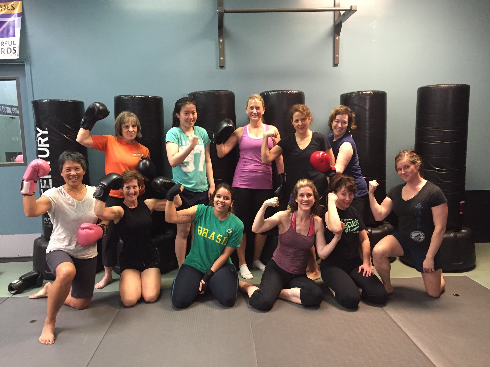 kickboxing students of various ages, races, genders, flexing arms and smiling